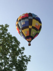 Bev Shaffer - When It's Been a Stressful Week -Multi-Color Hot Air Balloon over Trees